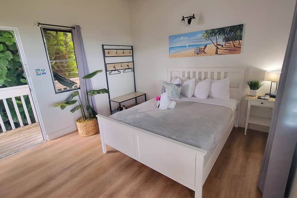 Bright bedroom with white bed, wooden floor, beach artwork, and sliding glass door