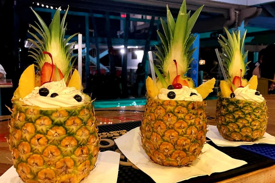 Three decorative pineapple cocktails with whipped cream, cherries, and tropical drinks poolside at night