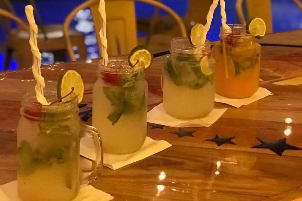 Colorful tropical cocktails with lemon slices and striped straws served in mason jars on wooden bar