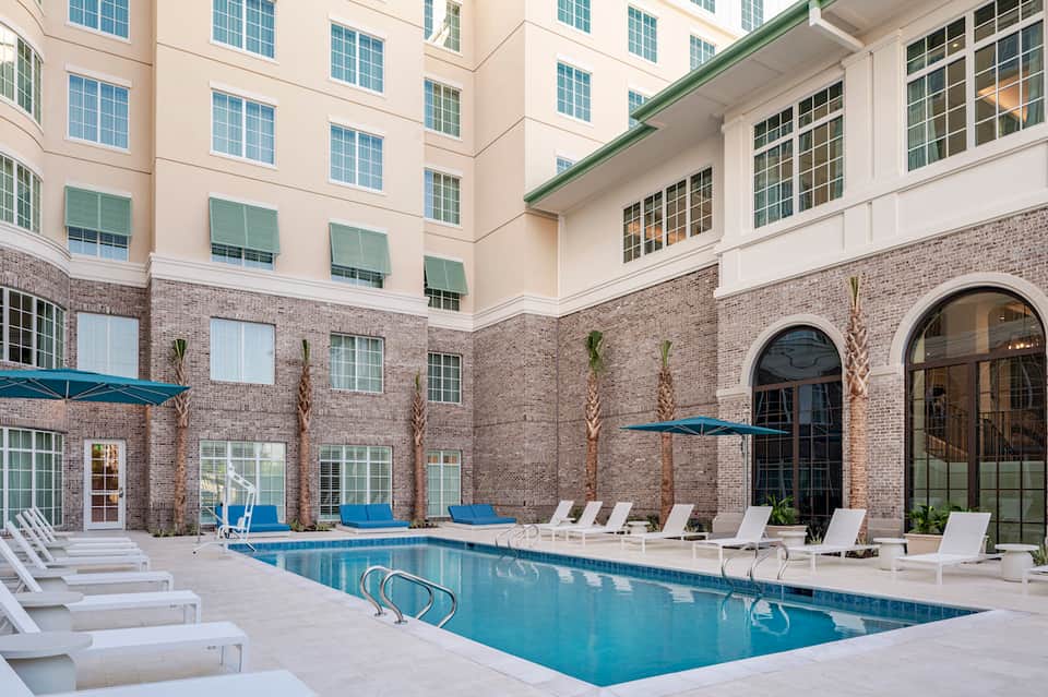 Indoor courtyard pool surrounded by brick building, white lounge chairs, and potted plants