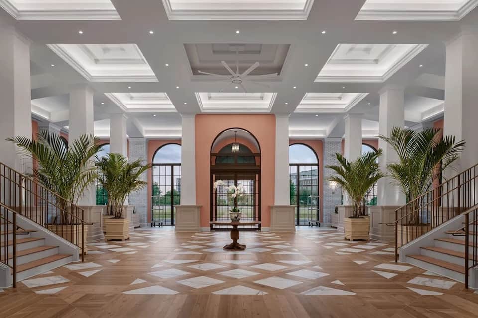 Elegant entrance hall with skylights, palm plants, marble floors, arched doorway, and dual staircases