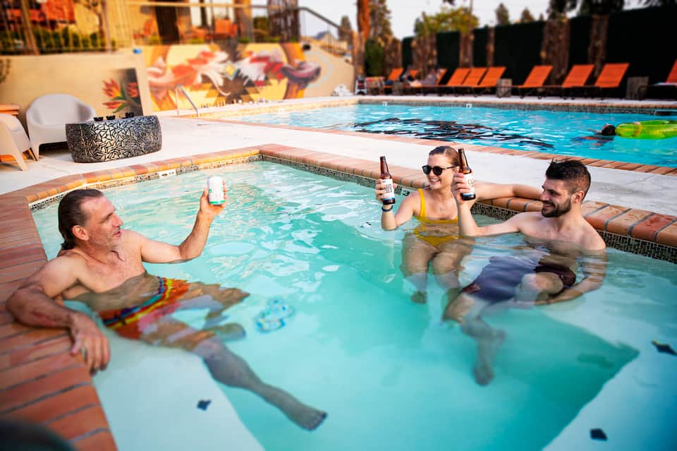 Three guests enjoying drinks in a shallow pool at a resort with colorful mural backdrop