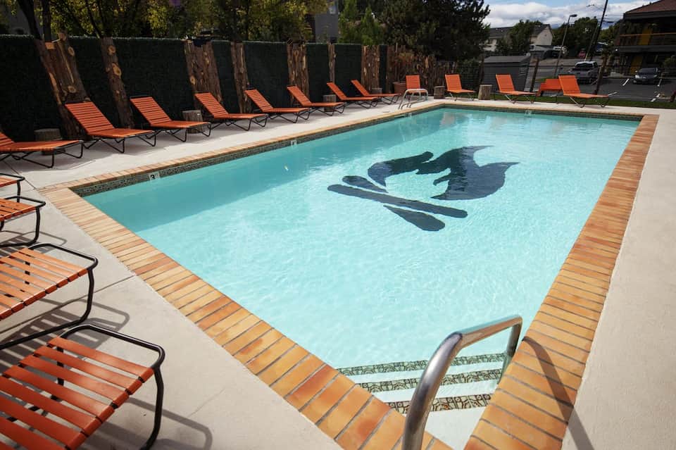 Resort swimming pool with orange lounge chairs, tall hedges, and mountains in background