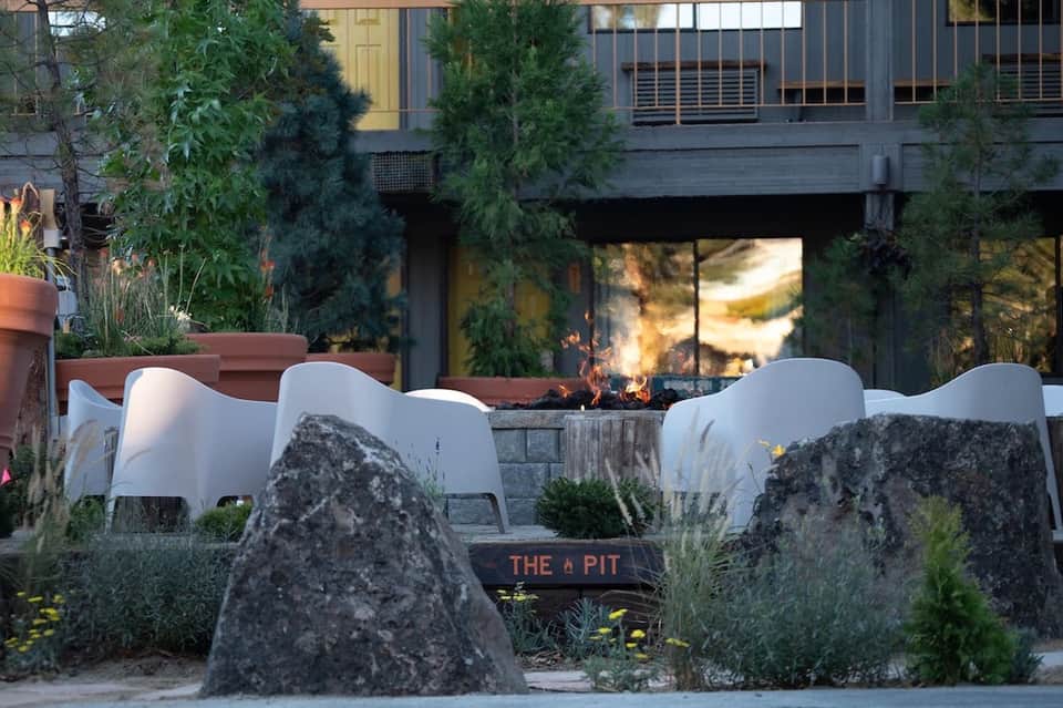 Outdoor fire pit seating area with white modern chairs and natural stone features at dusk