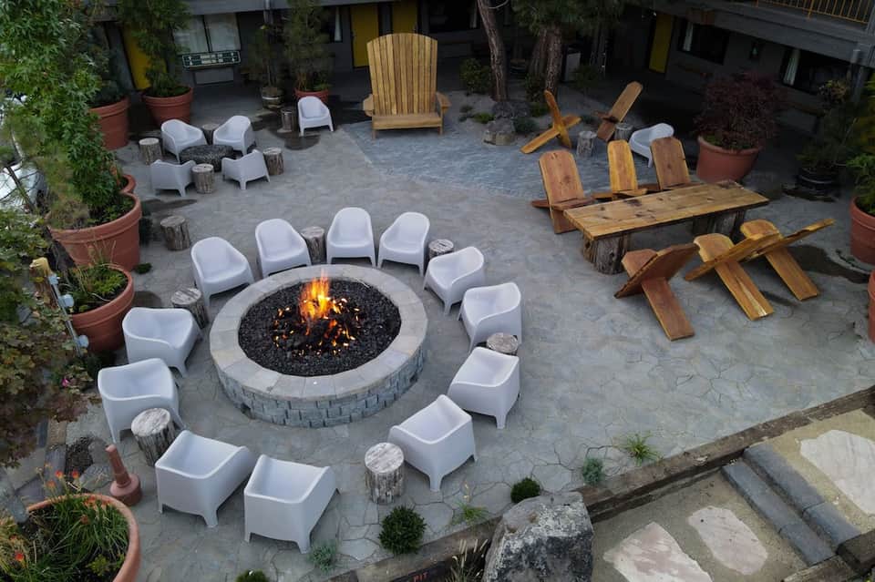 Outdoor fire pit area with white modern chairs and rustic wooden seating on stone patio