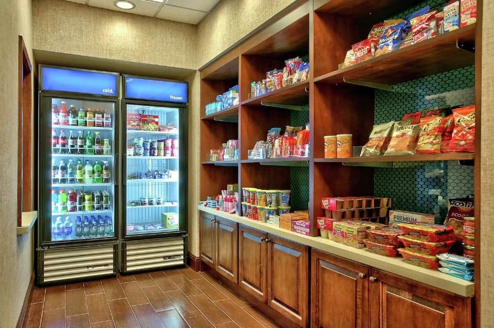 Hotel convenience store with refrigerated beverage cases and wooden shelving stocked with snacks and merchandise