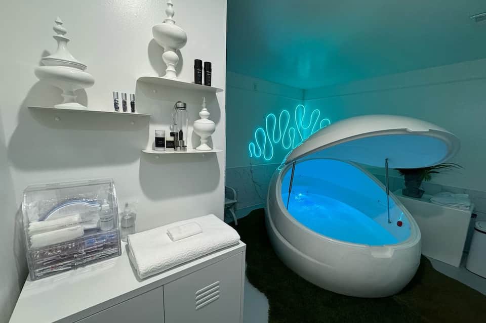 Modern spa bathroom with white shelving, cosmetics display, and glowing blue soaking tub