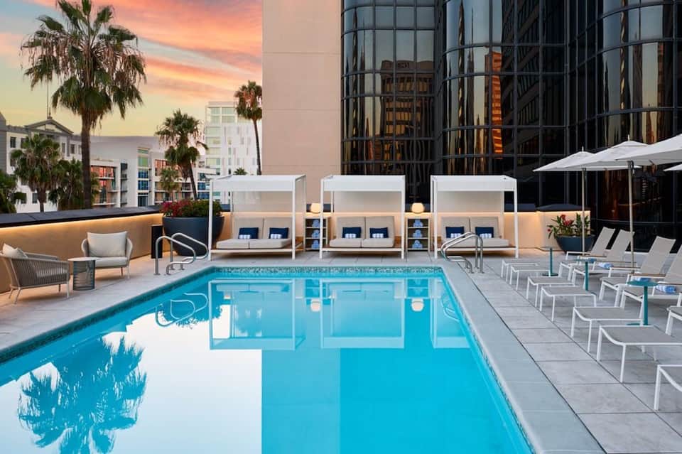 Modern rooftop pool at sunset with white cabanas, lounge chairs, and downtown city skyline views