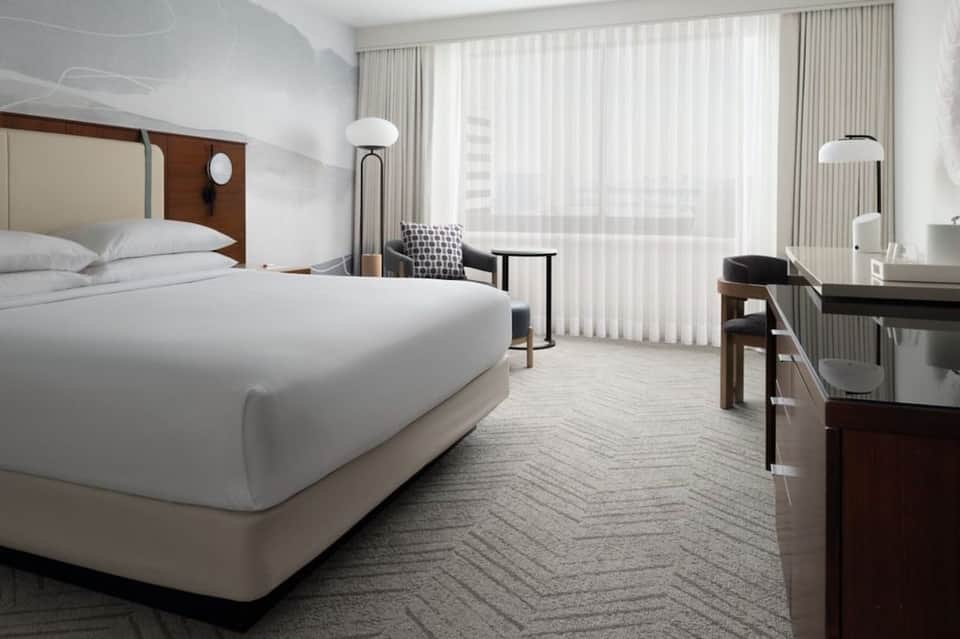 Modern hotel bedroom with king bed, floor-to-ceiling windows, and contemporary furnishings