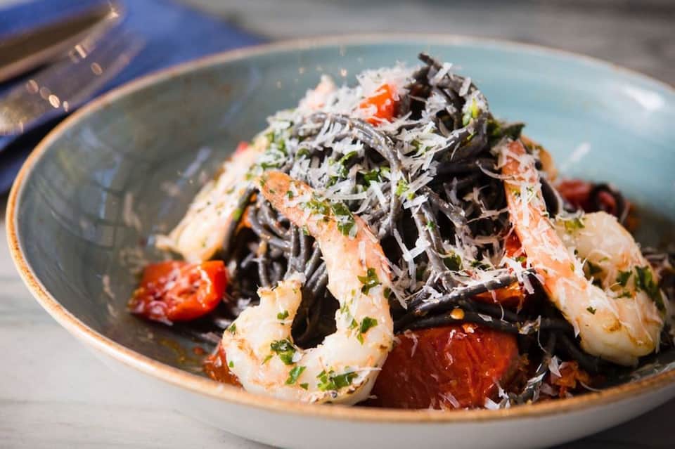 Gourmet seafood dish with shrimp, noodles, and garnish on a light blue plate