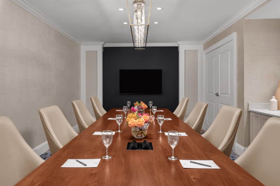 Formal boardroom with long wooden table, cream chairs, and flat-screen TV