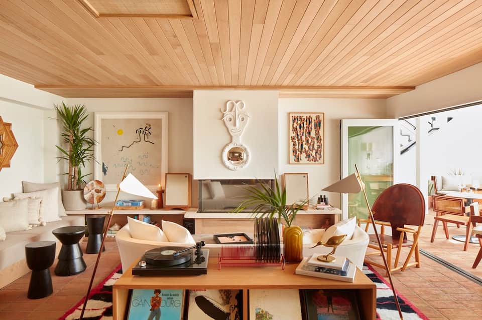 Mid-century modern living room with wood ceiling, blue sofa, plants, wall art, and open floor plan