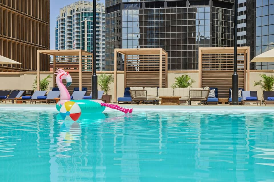 Vibrant turquoise rooftop pool with inflatable flamingo float and colorful beach ball, city skyline views
