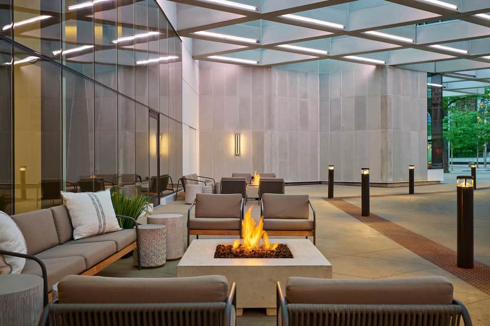 Modern rooftop lounge with fire pit, contemporary seating, and glass walls overlooking city skyline