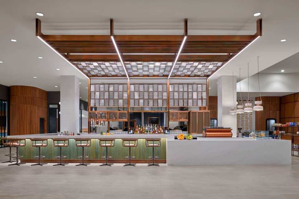 Contemporary hotel café with wooden lattice design, white counter, and modern pendant lighting