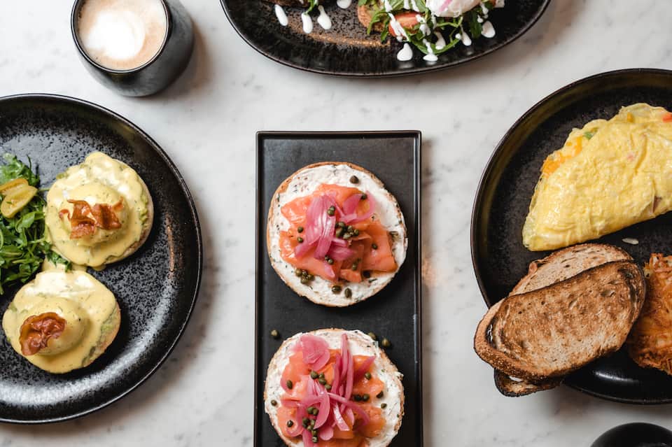 Appetizers on black plates including eggs Benedict and smoked salmon toast