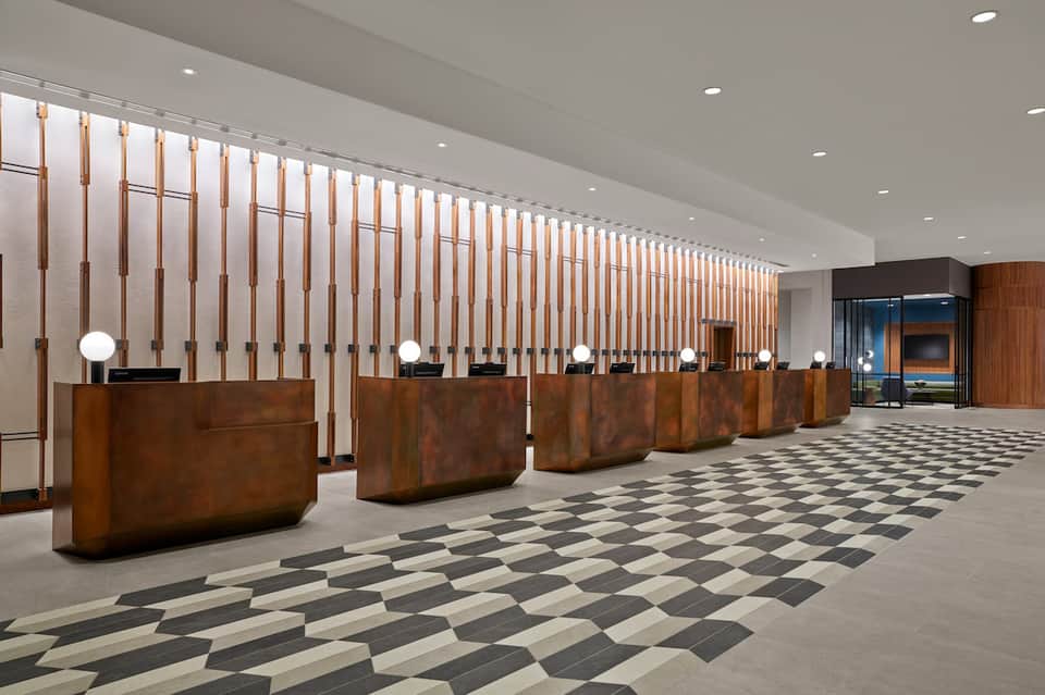 Hotel lobby with multiple wooden reception desks and vertical copper slat wall design