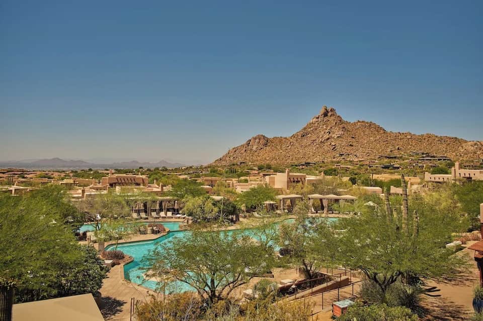 Desert resort with turquoise pool, earth-toned architecture, desert landscaping, and dramatic rock formation backdrop