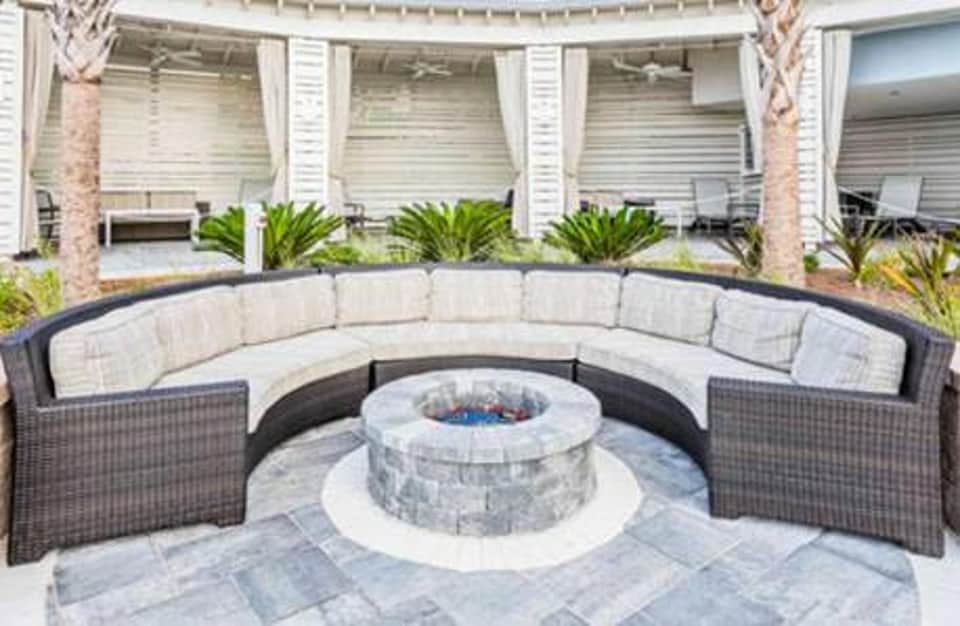 Curved outdoor seating area with cushions around fire pit surrounded by white pillars and palm trees