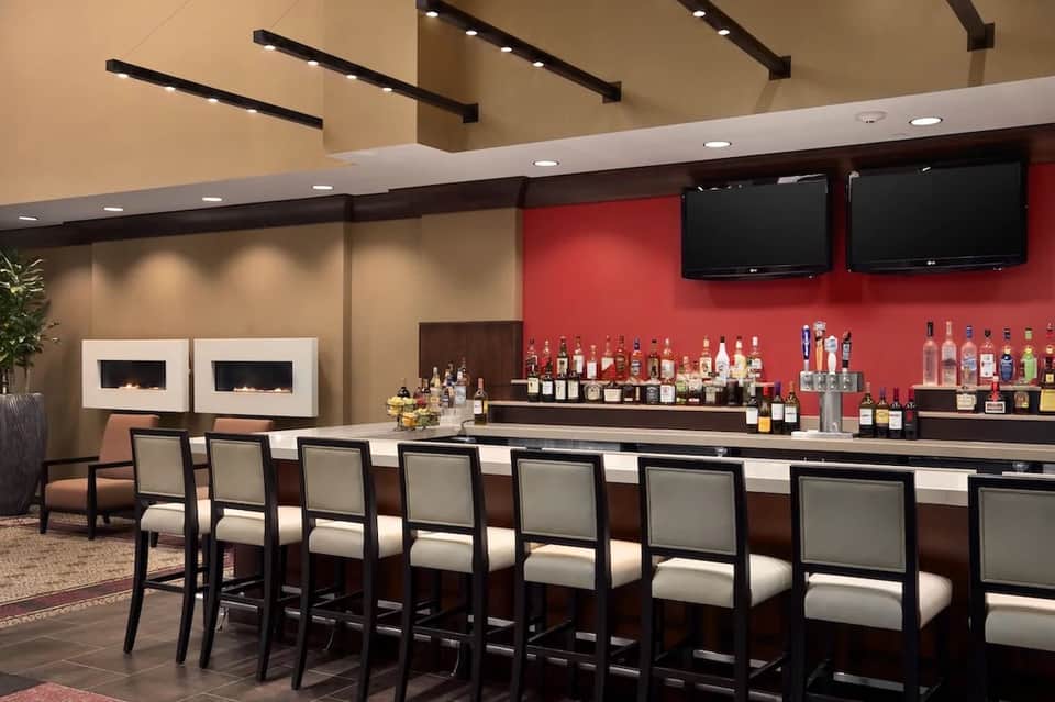 Hotel bar with red accent wall, built-in fireplace, stocked liquor shelves, and bar seating