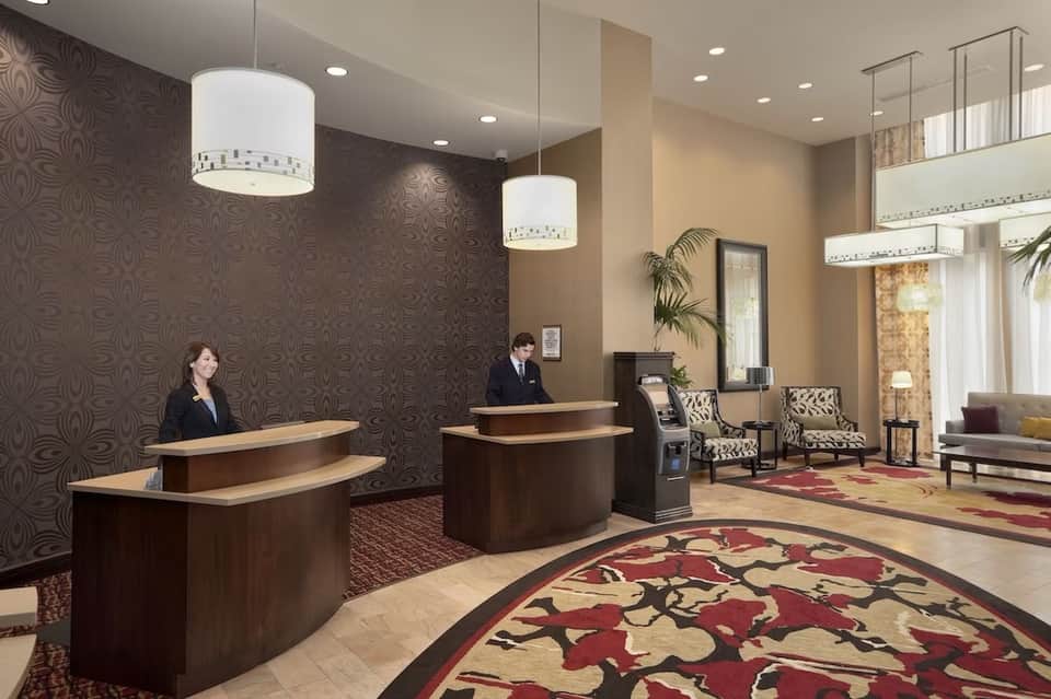 Hotel lobby with dual check-in desks, decorative wallpaper, pendant lights, and modern seating area