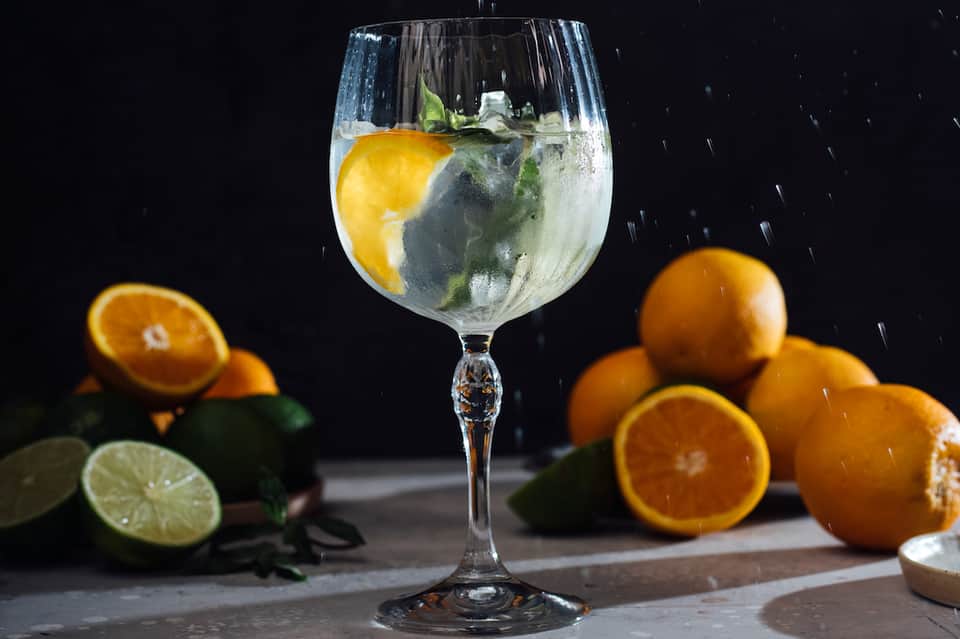 Refreshing gin and tonic cocktail with lemon slice and mint garnish surrounded by fresh citrus fruits