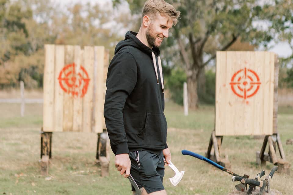 Man in black hoodie at axe-throwing range with wooden targets marked with red circles