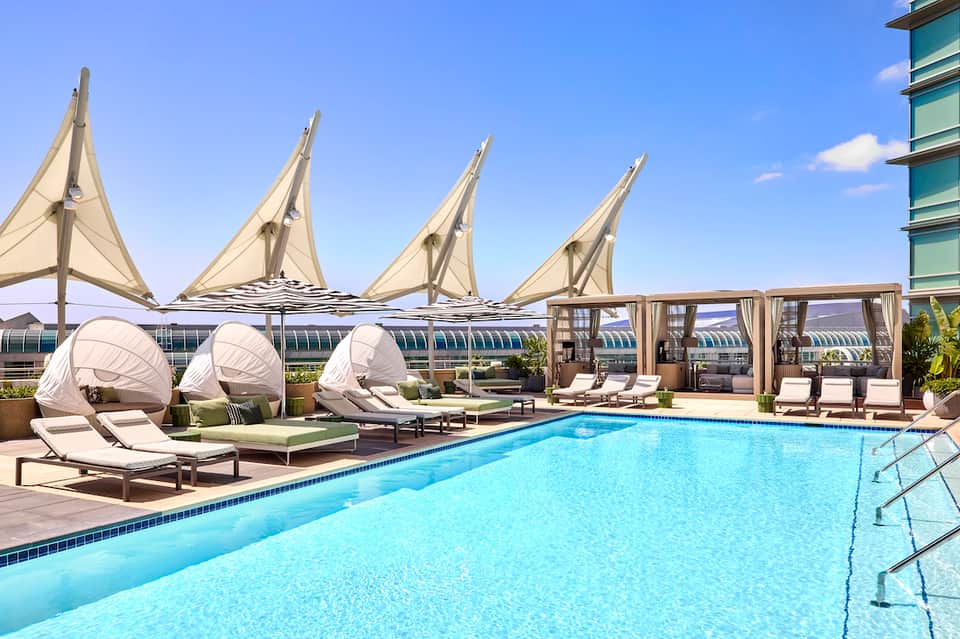Rooftop pool with sailcloth shade structures, loungers, and modern high-rise building backdrop