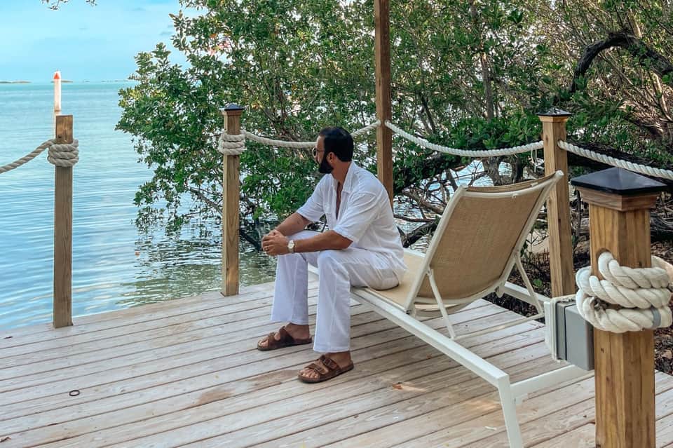 Man relaxing in lounge chair on wooden deck overlooking turquoise water with mangrove trees