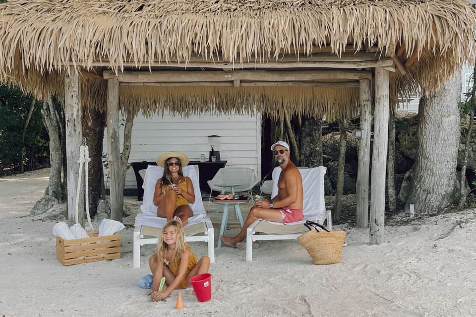 Thatched beach cabana with family relaxing in white lounge chairs overlooking ocean