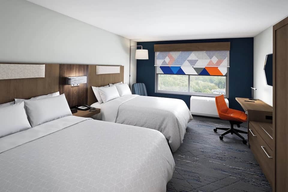 Modern hotel room with two queen beds, dark blue accent wall, and geometric window treatments