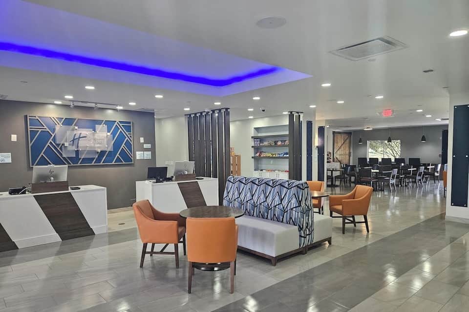 Contemporary hotel lobby featuring blue accent lighting, orange chairs, reception desk, and modern decor