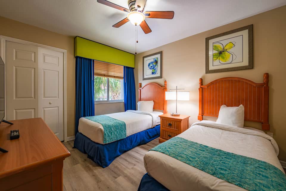 Colorful hotel room with two twin beds with orange headboards and teal bedding accents