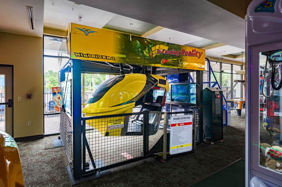 Arcade game room featuring yellow racing simulator machine and colorful gaming cabinets