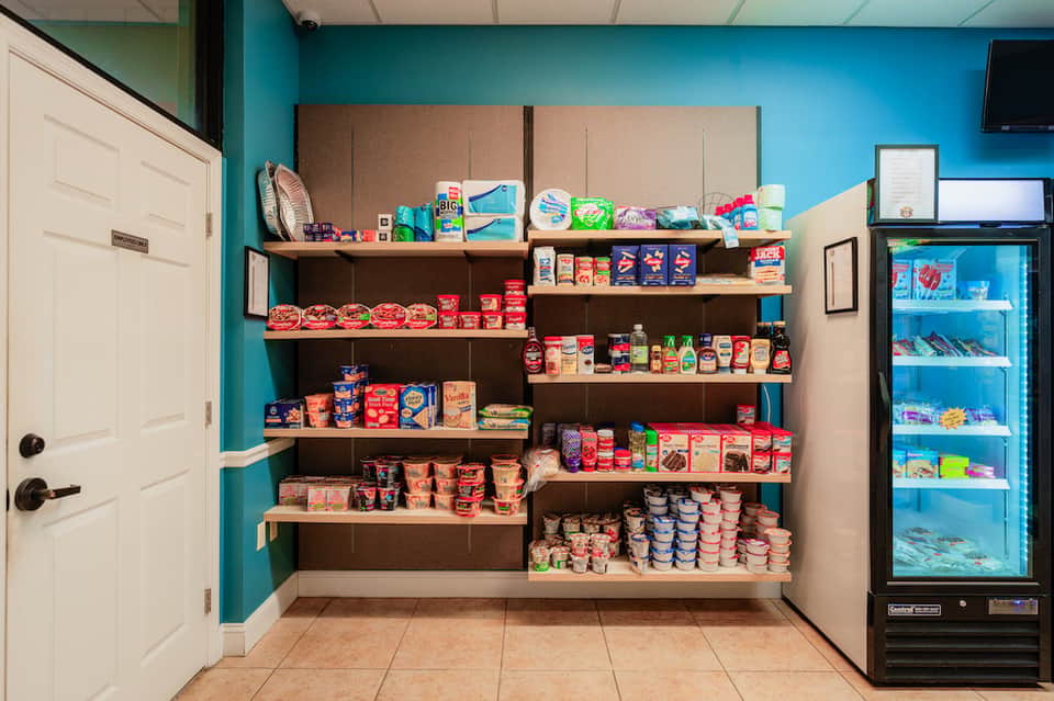 Hotel convenience store with teal walls, stocked shelves of snacks and beverages, refrigerator