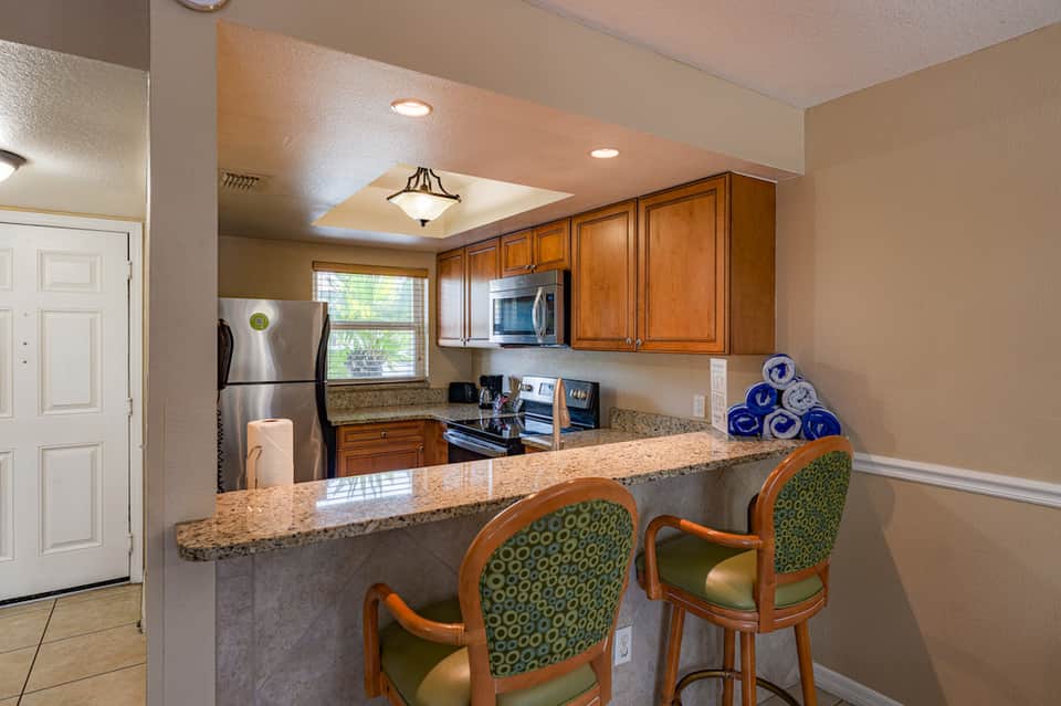 Hotel suite kitchenette with wooden cabinets, granite countertop, and patterned bar stools
