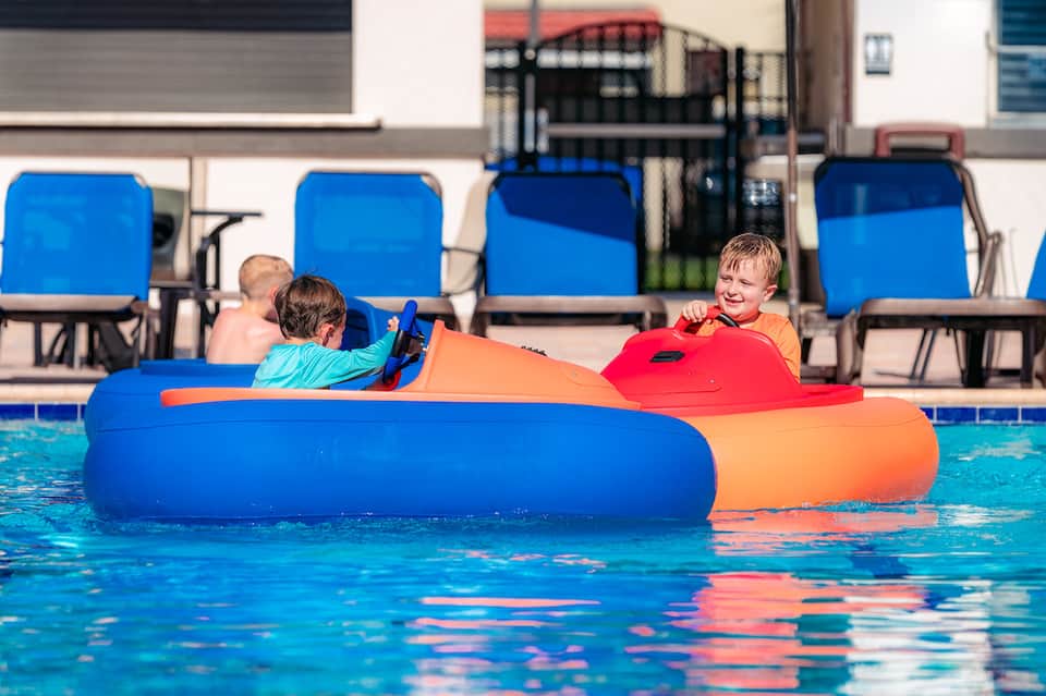 Children playing on colorful inflatable raft in bright blue swimming pool with lounge chairs