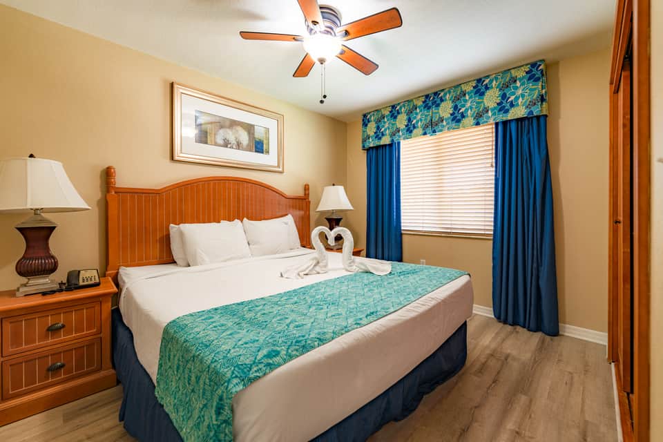 Bedroom with wooden bed frame, orange wood accents, blue curtains, and turquoise bedding