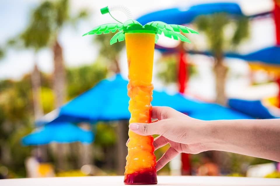 Colorful tropical drink with green palm leaf garnish held at pool area