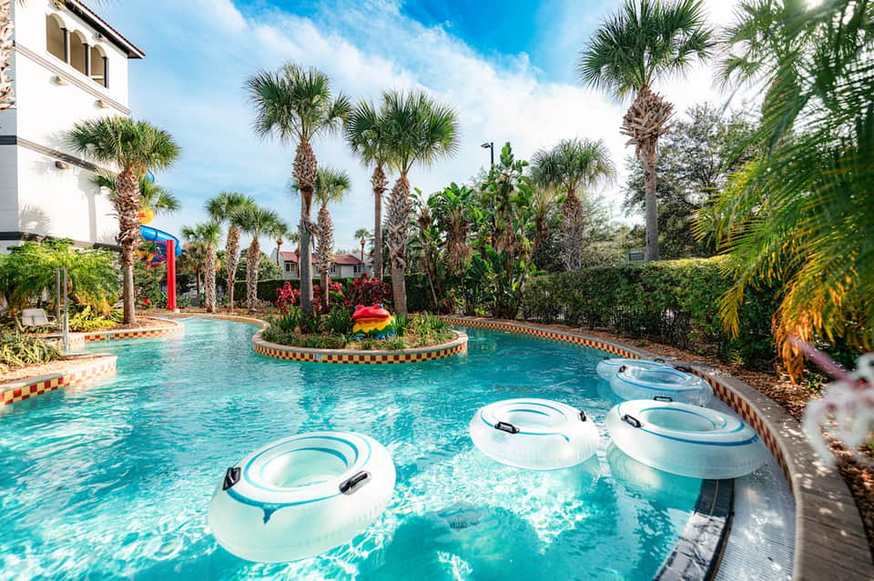 Resort pool with white float rings, palm trees, colorful decorative elements, and lounging areas