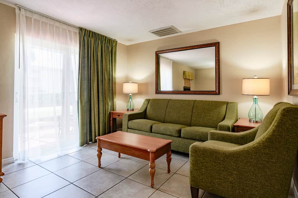 Cozy resort suite living room with green sofa, wooden table, and balcony access