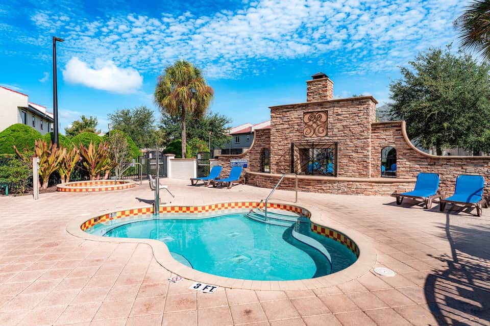 Spa hot tub with decorative border, blue lounge chairs, and brick building with palm trees
