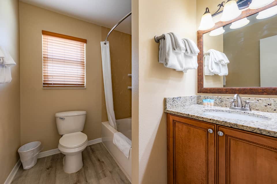 Modern bathroom with granite countertop, wooden vanity, white towels, and tiled shower area