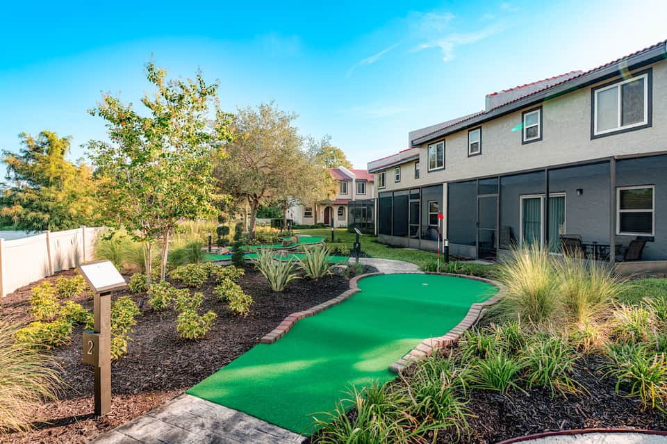 Miniature golf course with bright green playing surface, landscaping, and residential buildings
