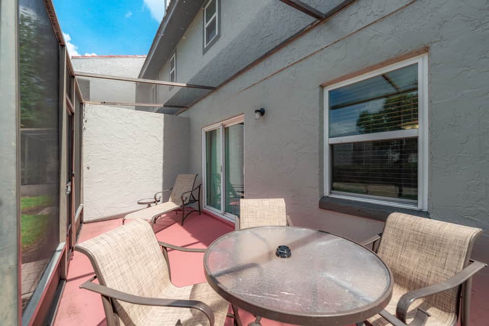 Pink concrete patio with metal outdoor furniture and round table overlooking fenced residential area