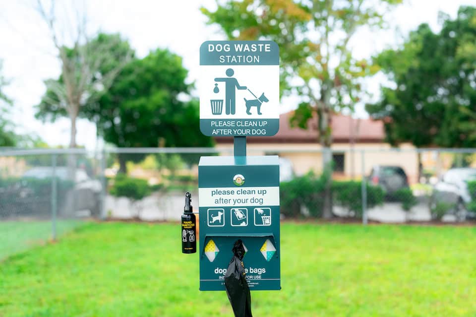 Dog waste station sign in park with supplies and trash receptacle