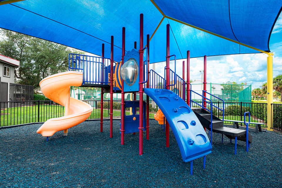 Colorful playground with blue canopy, orange spiral slide, and climbing structures in resort setting
