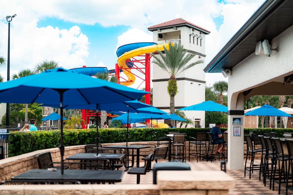 Outdoor resort area with blue umbrellas, water slide, and palm trees near the pool