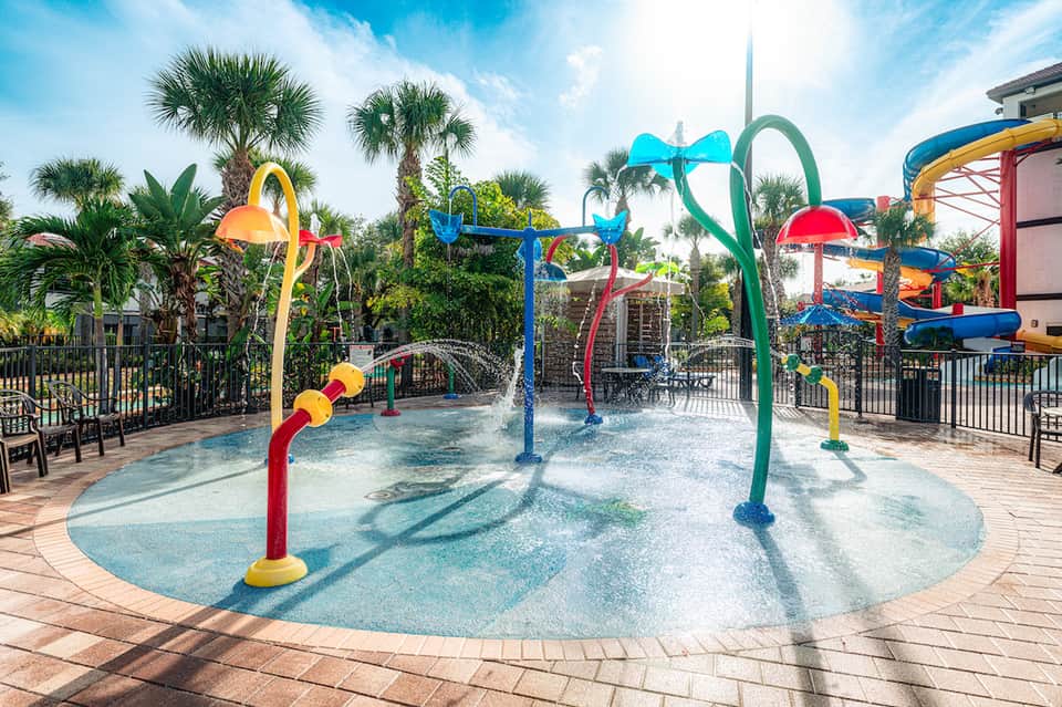 Colorful splash pad with interactive water fountains and sprayers surrounded by palm trees at resort