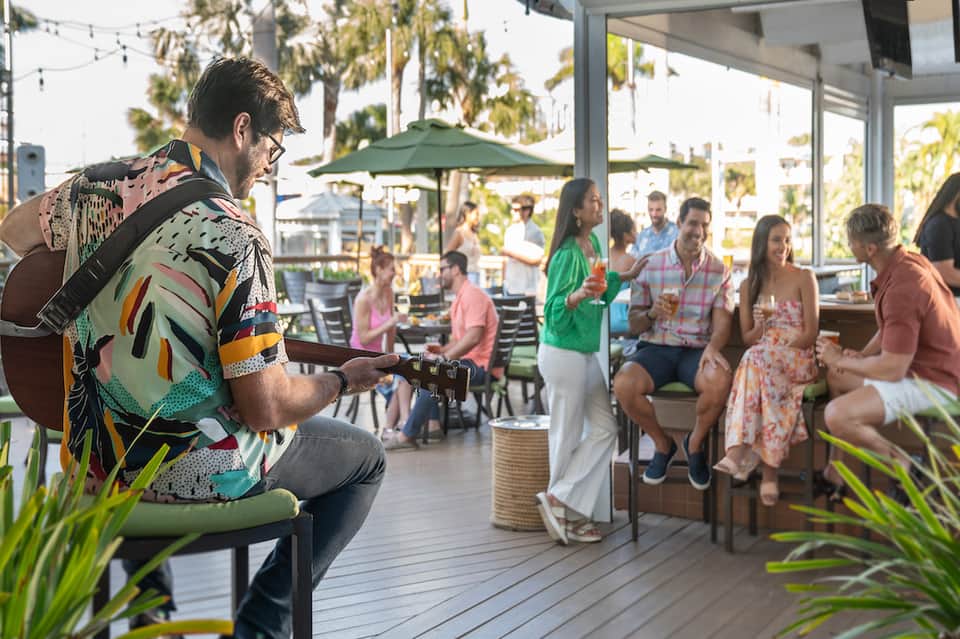 Live musician performing guitar for guests at outdoor resort venue with palm trees